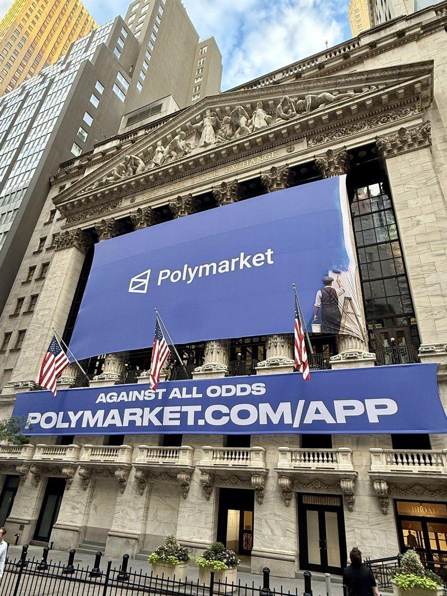 Polymarket 배너와 브랜딩이 있는 증권거래소 건물의 거리 사진
